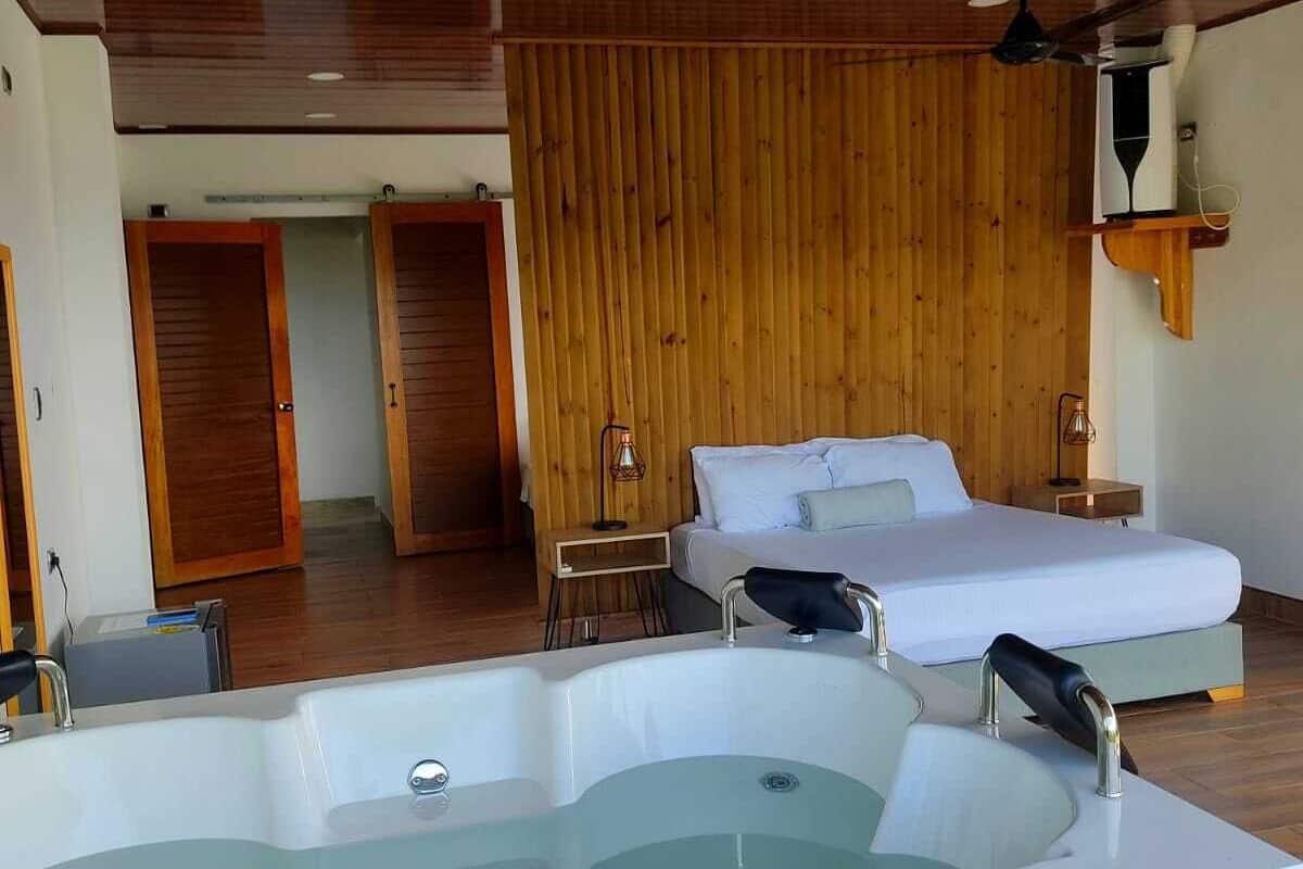 Een moderne slaapkamer met een ruime badkuip, twee bedden, houten lambrisering en een plafondventilator.