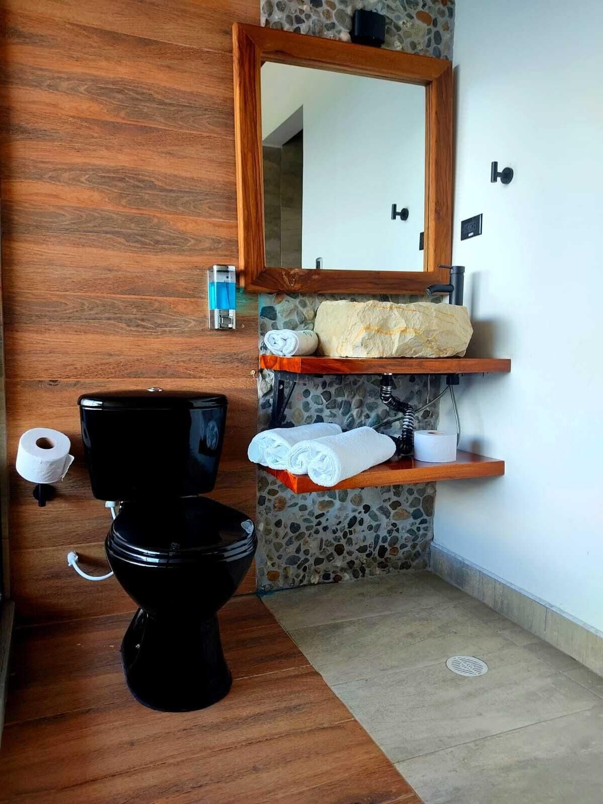 A bathroom with a black toilet, a wooden vanity, a stone backsplash, and a wooden floor.