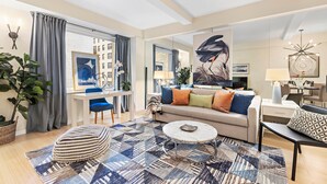 Un salon moderne comprenant un canapé, une table basse et un pouf, un coin repas avec des chaises, et une grande fenêtre agrémentée de rideaux.