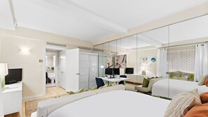 Une chambre d’hôtel moderne, dotée d’un grand lit, d’un bureau, d’une télévision et d’une salle de bain visible à travers une porte ouverte.