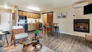 A modern living room with a fireplace, a dining area, and a kitchen with wooden cabinets and a microwave.