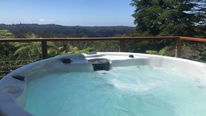 Relax in the hot tub on the balcony with a serene view of the lush landscape.