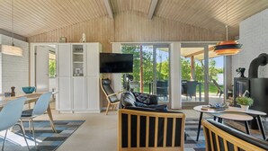 Un interior moderno con techo de madera, una zona de comedor con sillas y una mesa, un sofá, un televisor y una chimenea.
