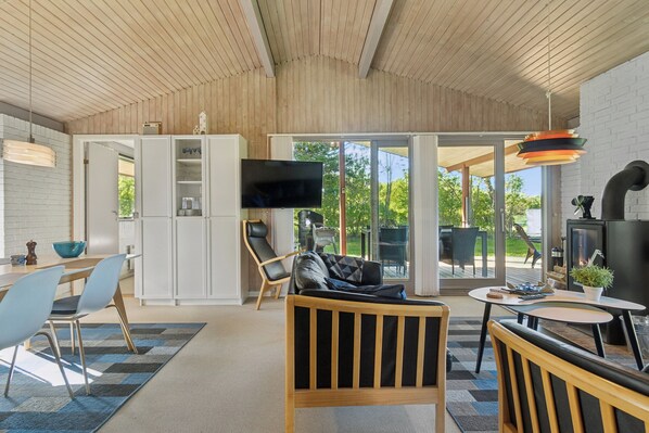 Un intérieur moderne avec un plafond en bois, un coin repas comprenant des chaises et une table, un canapé, un téléviseur et une cheminée.