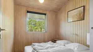 Una habitación con paneles de madera, una cama, una ventana y un cuadro en la pared.