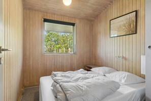 A wooden-paneled room with a bed, a window, and a framed picture on the wall.