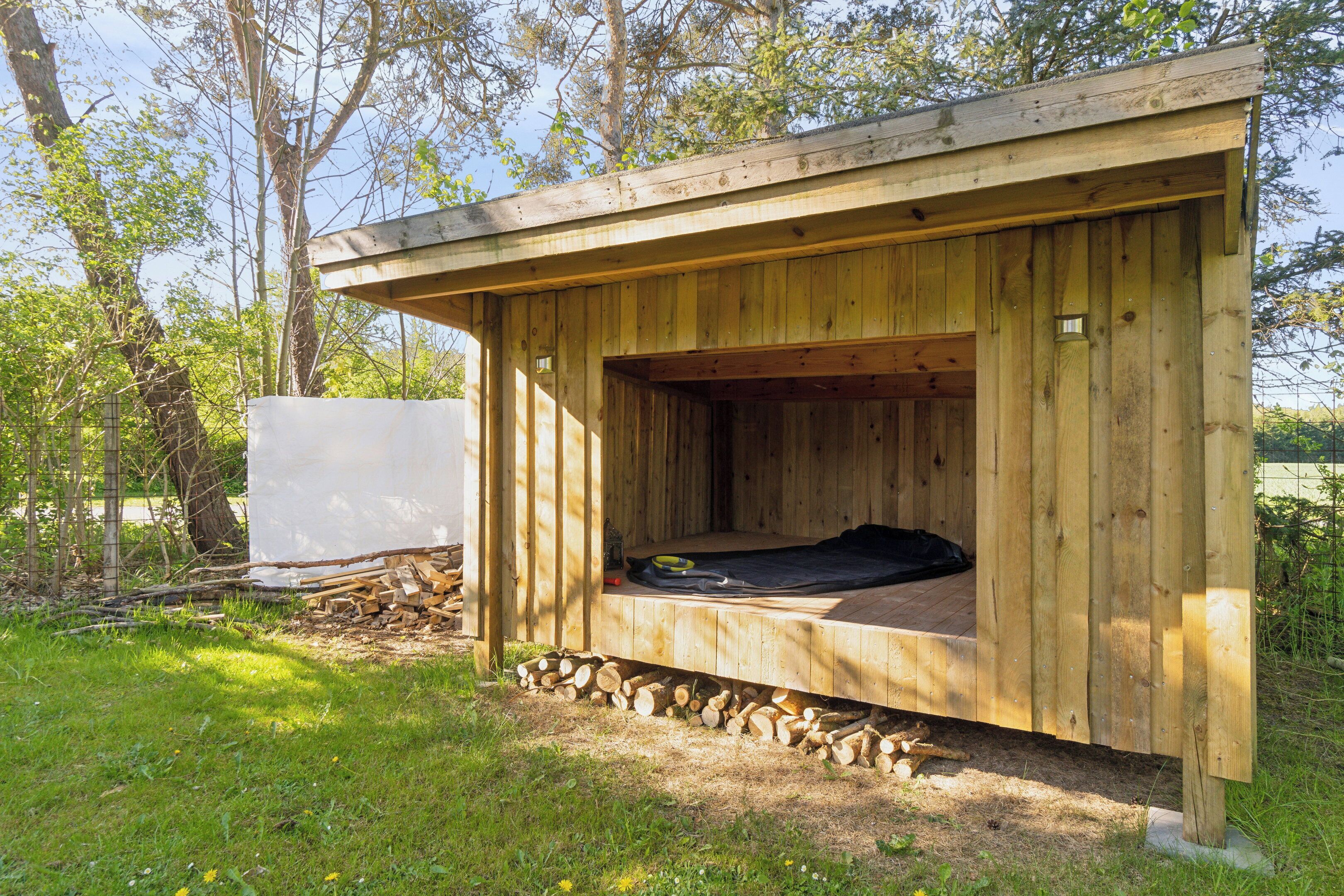 Eine Holzhütte mit Schlafkoje, einer kleinen abgeschlossenen Nische und einem Holzstoß davor.