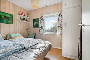 Un dormitorio con paredes de madera, una cama con colcha estampada, una ventana con cortinas florales y una puerta con una toalla colgada.