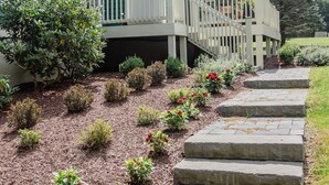 A green house with a white porch and a stone pathway leading to a white fence. - Green Acres - Lake Access - Hot tub - Fire pit (Swanton)