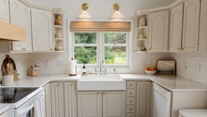 A kitchen with white cabinetry, a double sink, and a window with a view of greenery. - Green Acres - Lake Access - Hot tub - Fire pit (Swanton)