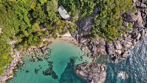 Vue aérienne d’une zone côtière avec des eaux turquoise limpides, des côtes rocheuses et une végétation luxuriante.