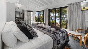 Une chambre moderne avec un grand lit, une petite table, une chaise et une vue sur des palmiers et l’eau.