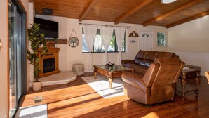 A cozy living room with a fireplace, leather sofa, wooden flooring, and a ceiling fan. - Near Yosemite & Lake & On Golf Course (Groveland)