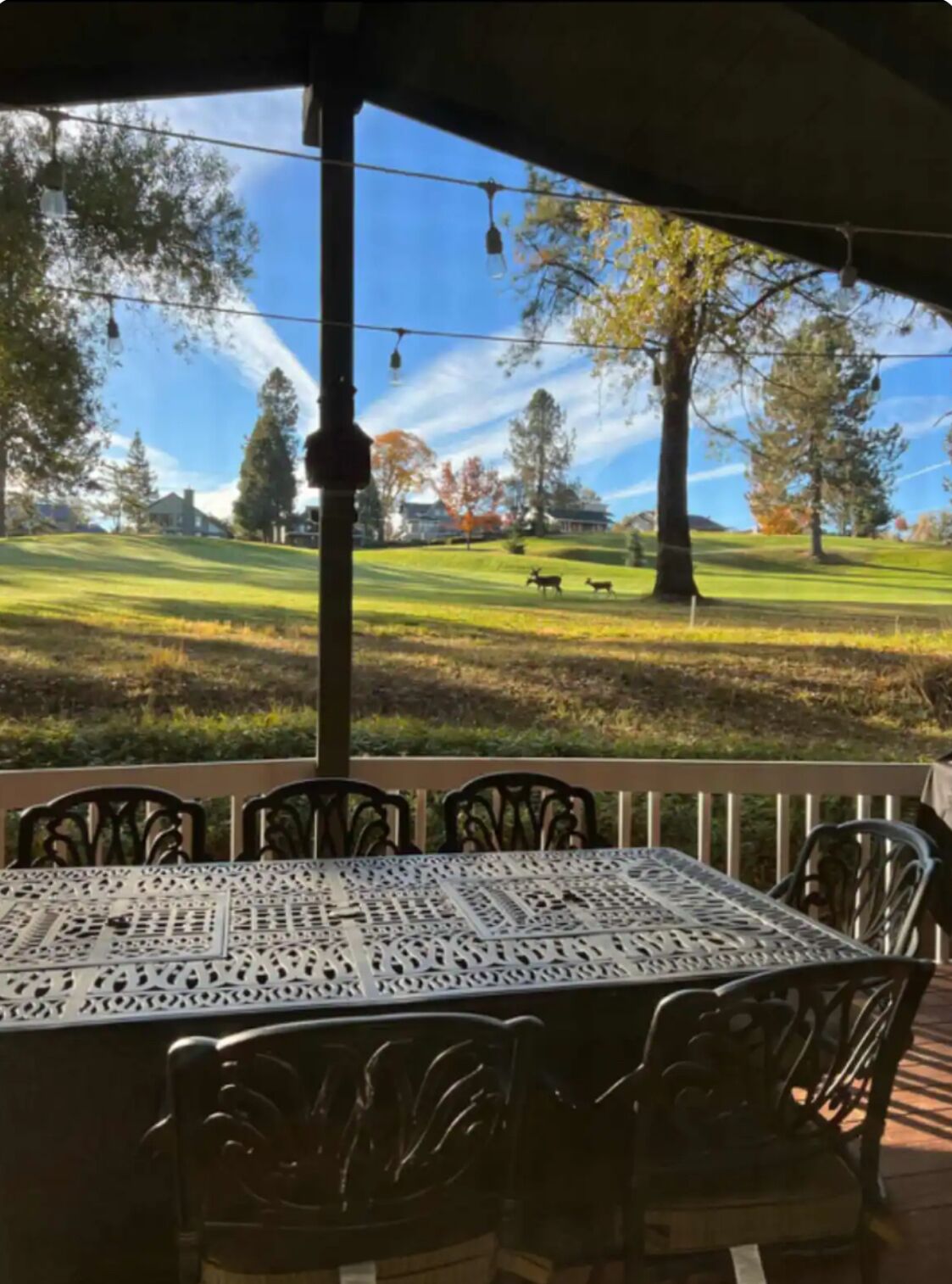 A covered patio with a table and chairs, overlooking a golf course with trees and a clear sky.