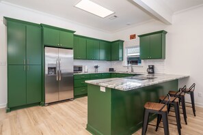 A modern kitchen with green cabinets, a stainless steel refrigerator, a marble island, and bar stools.