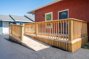 A wooden deck leading to a house with a red exterior, a blue door, and a window with green shutters.
