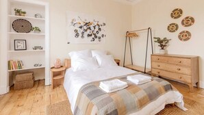 Ein ordentlich eingerichtetes Schlafzimmer mit einem Bett, einer hölzernen Kommode, einem Bücherregal und einer Wandlampe.