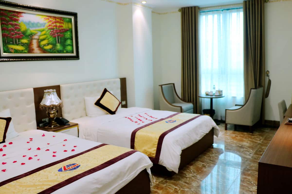 A hotel room with two beds, a nightstand with a lamp, a small table, two chairs, and a painting on the wall.