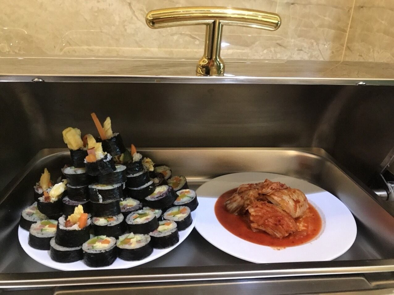 En buffé med sushirullar och en tallrik med kyckling i tomatsås.