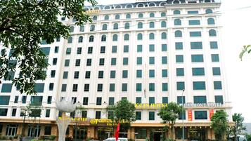 Un hotel de varios pisos con una entrada central, rodeado de vegetación y automóviles estacionados.