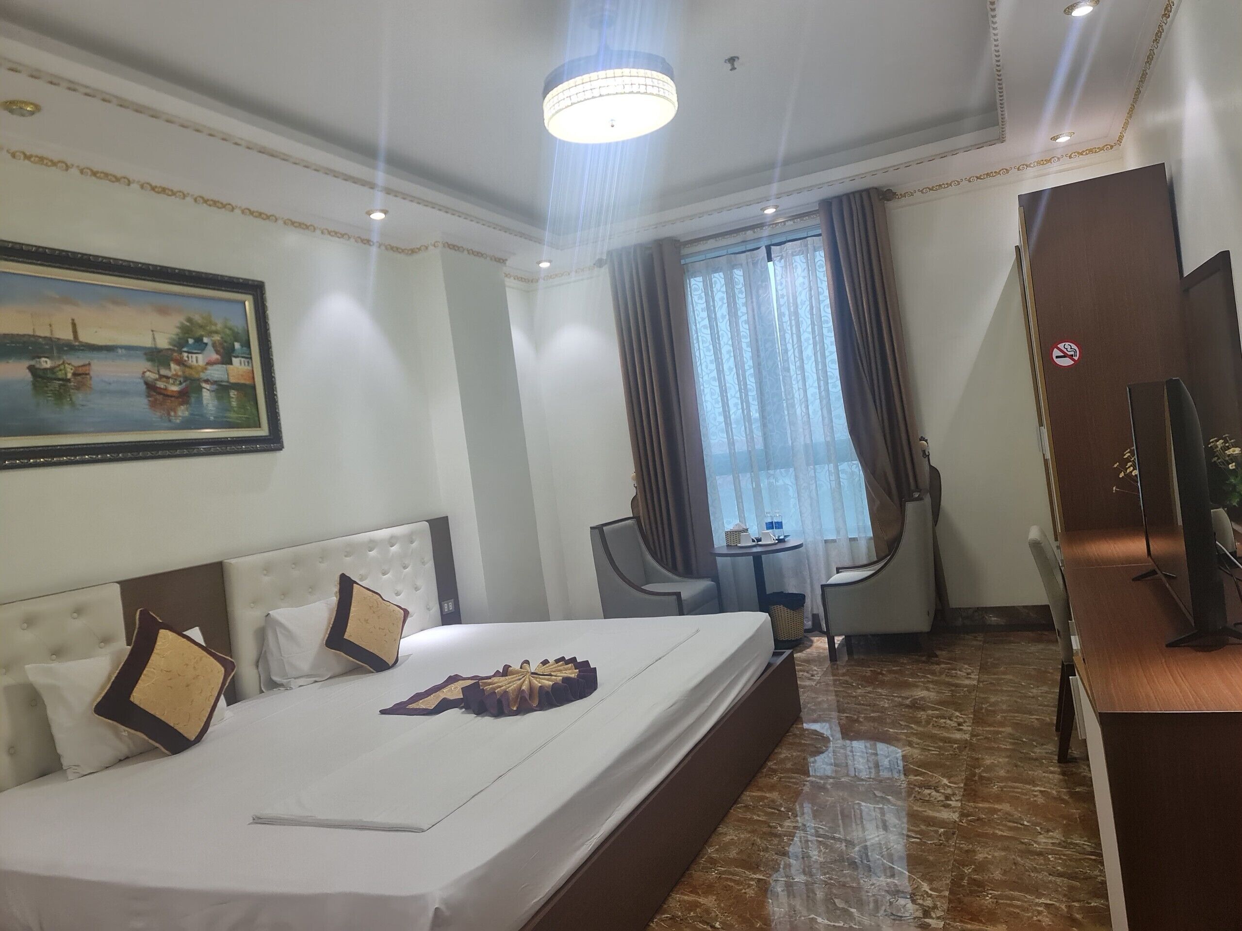 Une chambre d’hôtel avec un grand lit, un bureau, une chaise, une télévision et une fenêtre avec des rideaux.