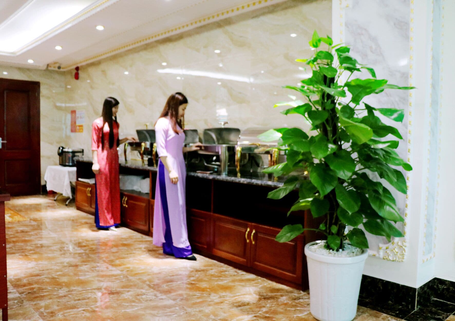 Un vestíbulo de hotel con piso de mármol, un mostrador de recepción y una gran planta en maceta.