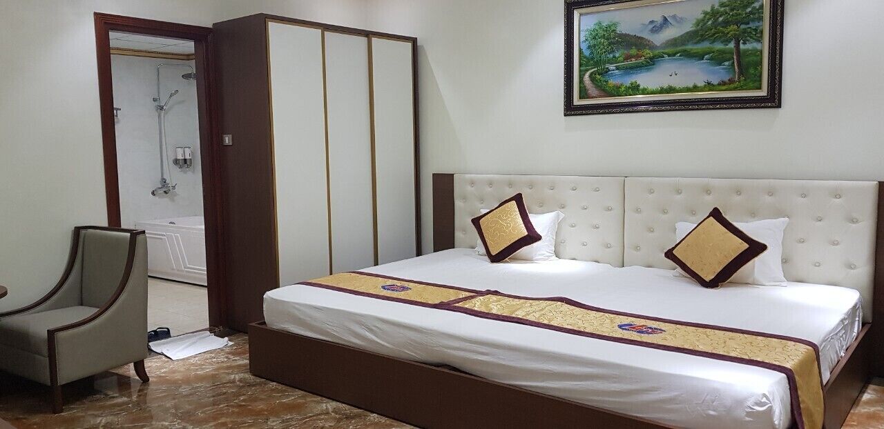 A hotel room with a bed, a chair, a wardrobe, and a painting on the wall.