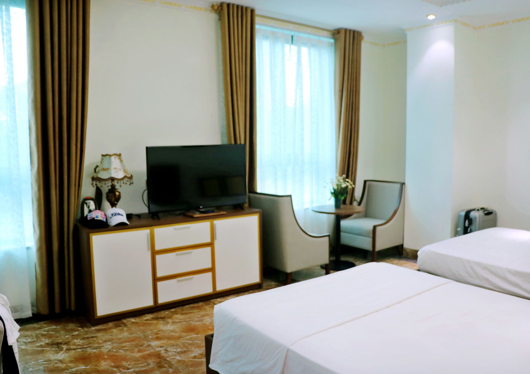 A hotel room with two beds, a TV on a wooden cabinet, a desk with a lamp, and a chair.