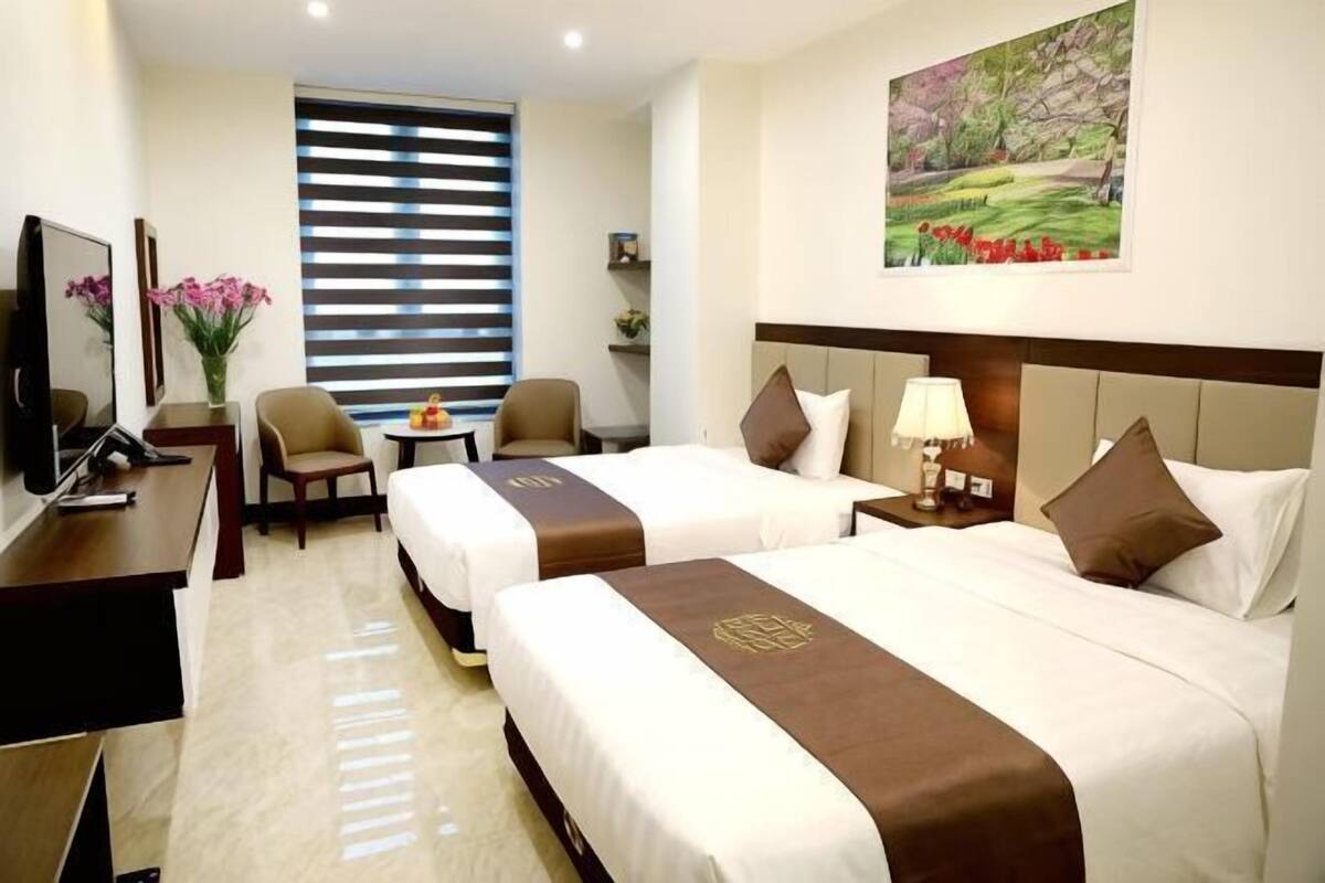 A hotel room with two beds, a desk, a chair, a TV, and a window with blinds.