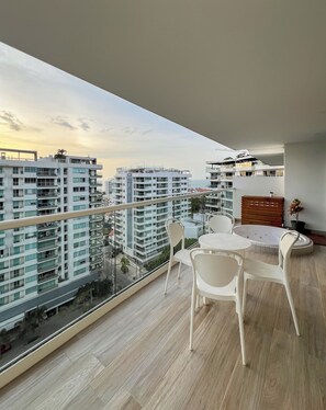 A balcony with a glass railing, a round table with chairs, and a wooden cabinet. - Exclusive oceanfront apartment featuring a private jacuzzi on the balcony (La Boquilla)