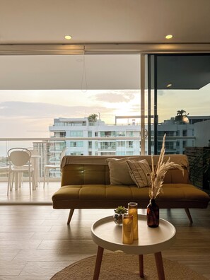 A modern living room with a sofa, a round table with drinks, and a view of a cityscape through large windows. - Exclusive oceanfront apartment featuring a private jacuzzi on the balcony (La Boquilla)