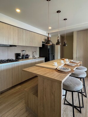 A modern kitchen with wooden cabinets, a central island with stools, pendant lighting, and a built-in stove. - Exclusive oceanfront apartment featuring a private jacuzzi on the balcony (La Boquilla)
