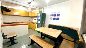Una pequeña kitchenette con un lavamanos, estufa y alacenas. En el centro, hay bancos de madera y una mesa.