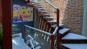 Una escalera con barandillas de metal que desciende a un nivel inferior, una pared de ladrillo y un cartel en la pared.