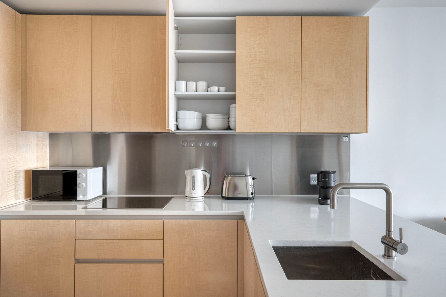 Una cucina moderna con mobili in legno, un lavello in acciaio inossidabile, un bollitore, un tostapane e un forno a microonde.