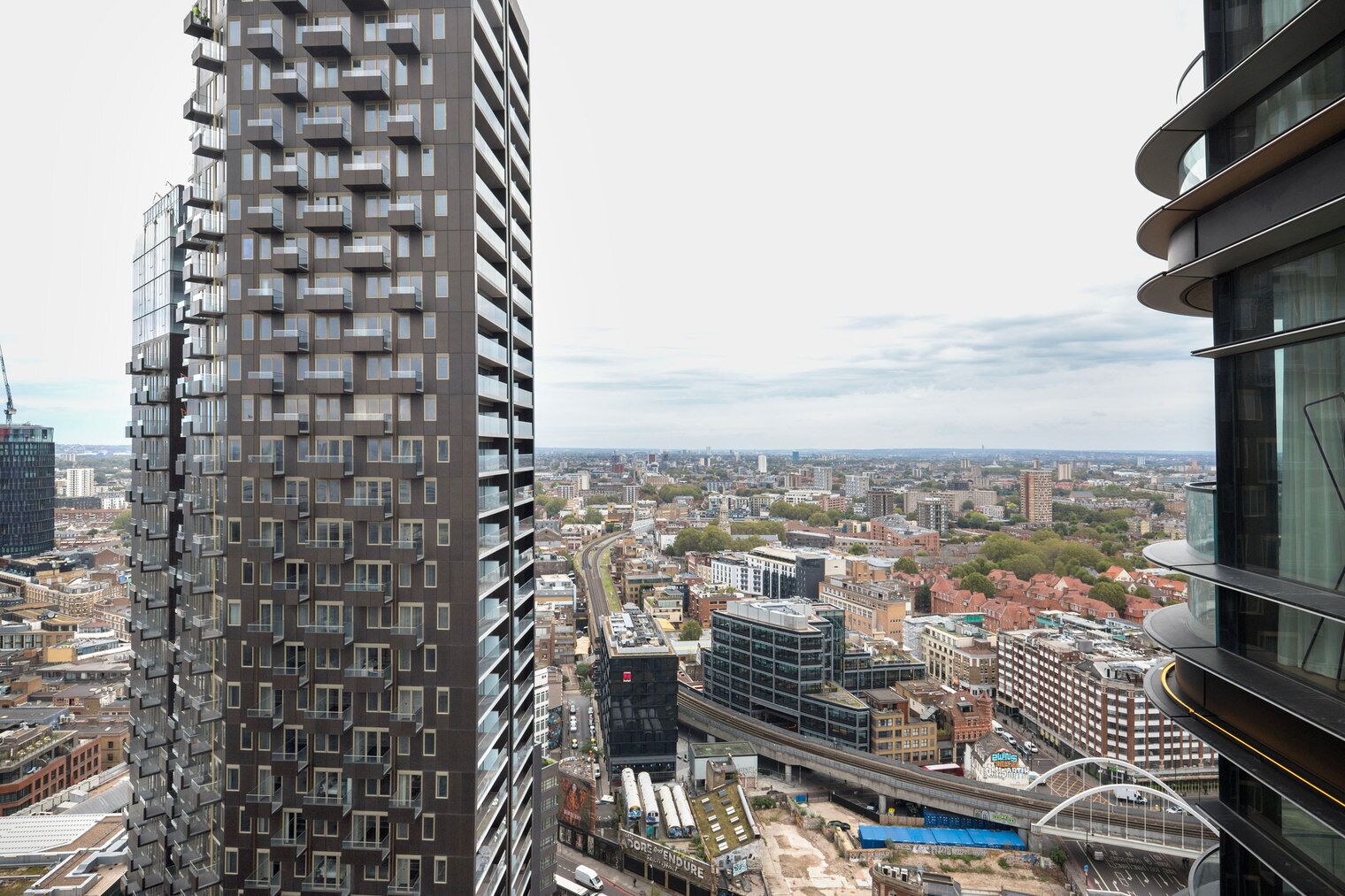 Een hoog gebouw met een modern architectonisch ontwerp, met tal van balkons en uitzicht op een stadsgezicht met verschillende gebouwen en infrastructuur.