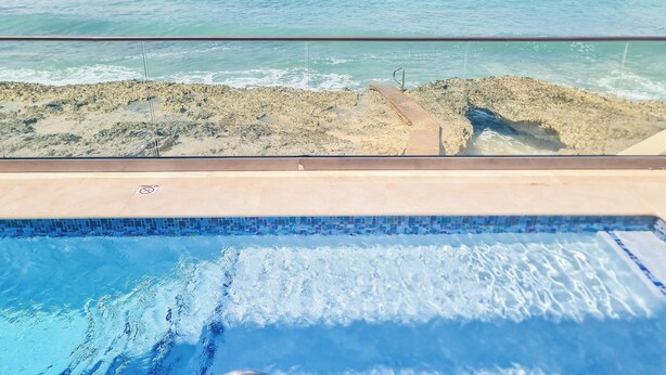 A pool with a view of the ocean and rocky shoreline. - Stunning views of Seven Mile Beach, luxurious rooftop and oceanfront pool. (West Bay)