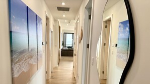 A hallway with wooden flooring, white walls, and large beach-themed paintings on the walls. - Stunning views of Seven Mile Beach, luxurious rooftop and oceanfront pool. (West Bay)