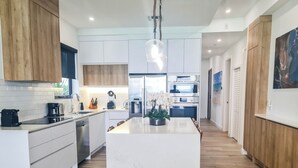 A modern kitchen with white cabinetry, a central island, and a built-in oven. - Stunning views of Seven Mile Beach, luxurious rooftop and oceanfront pool. (West Bay)
