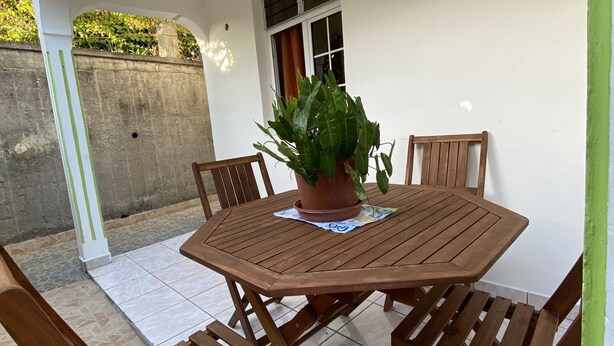 Une terrasse avec une table ronde en bois et quatre chaises en bois, une plante en pot et une fenêtre.