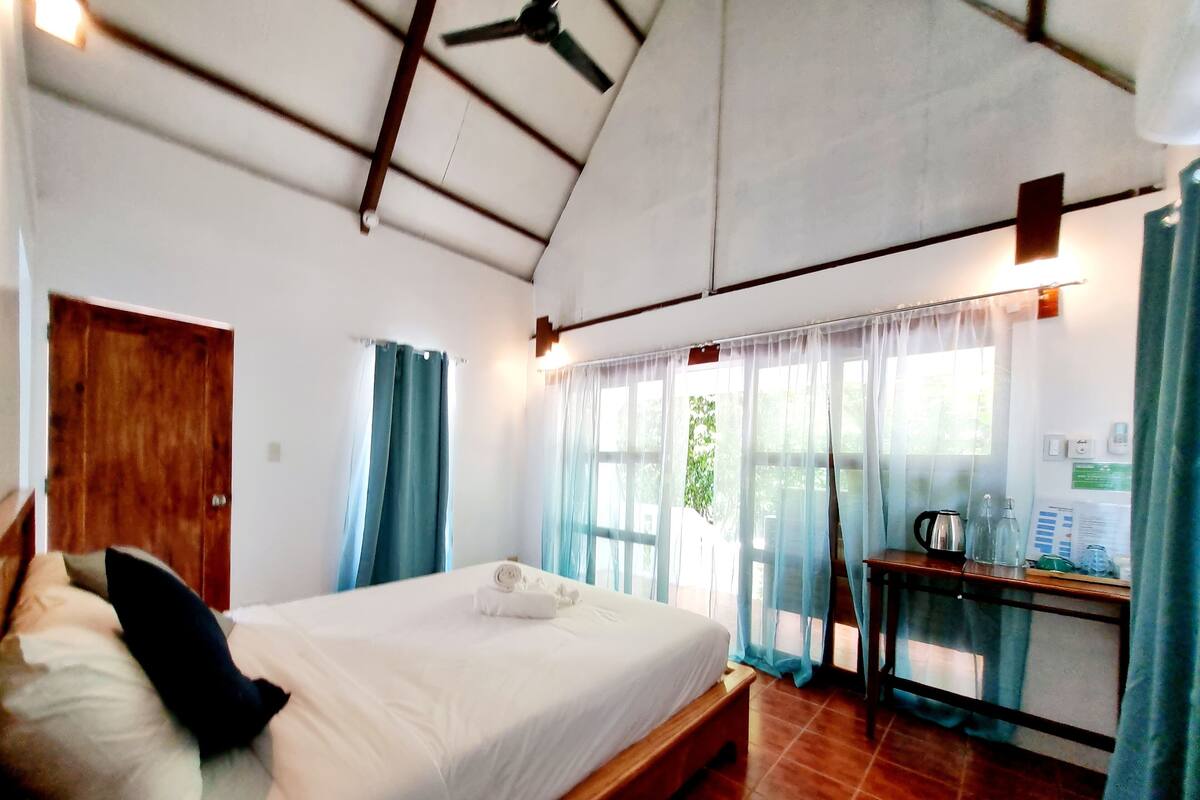 Une chambre à coucher avec un lit, un bureau en bois, une chaise et une fenêtre avec des rideaux.