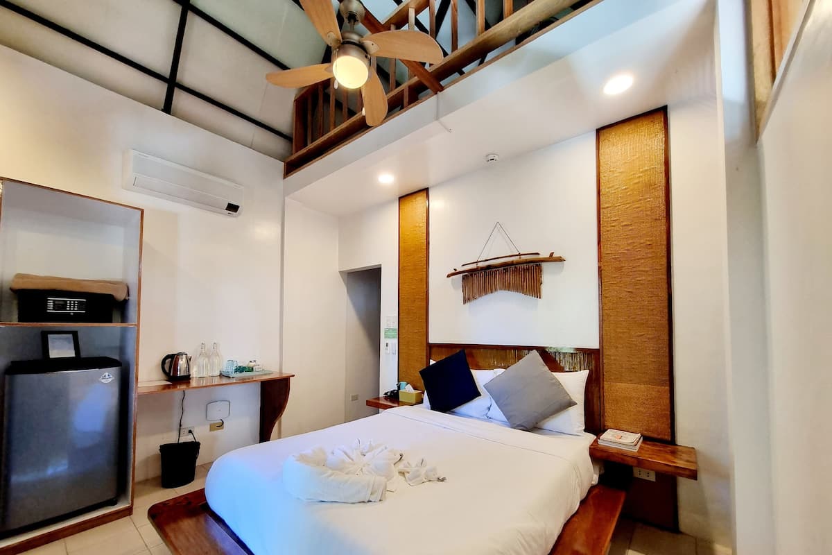 Une chambre d’hôtel équipée d’un lit, d’un bureau, d’un ventilateur de plafond et d’une étagère fixée au mur.