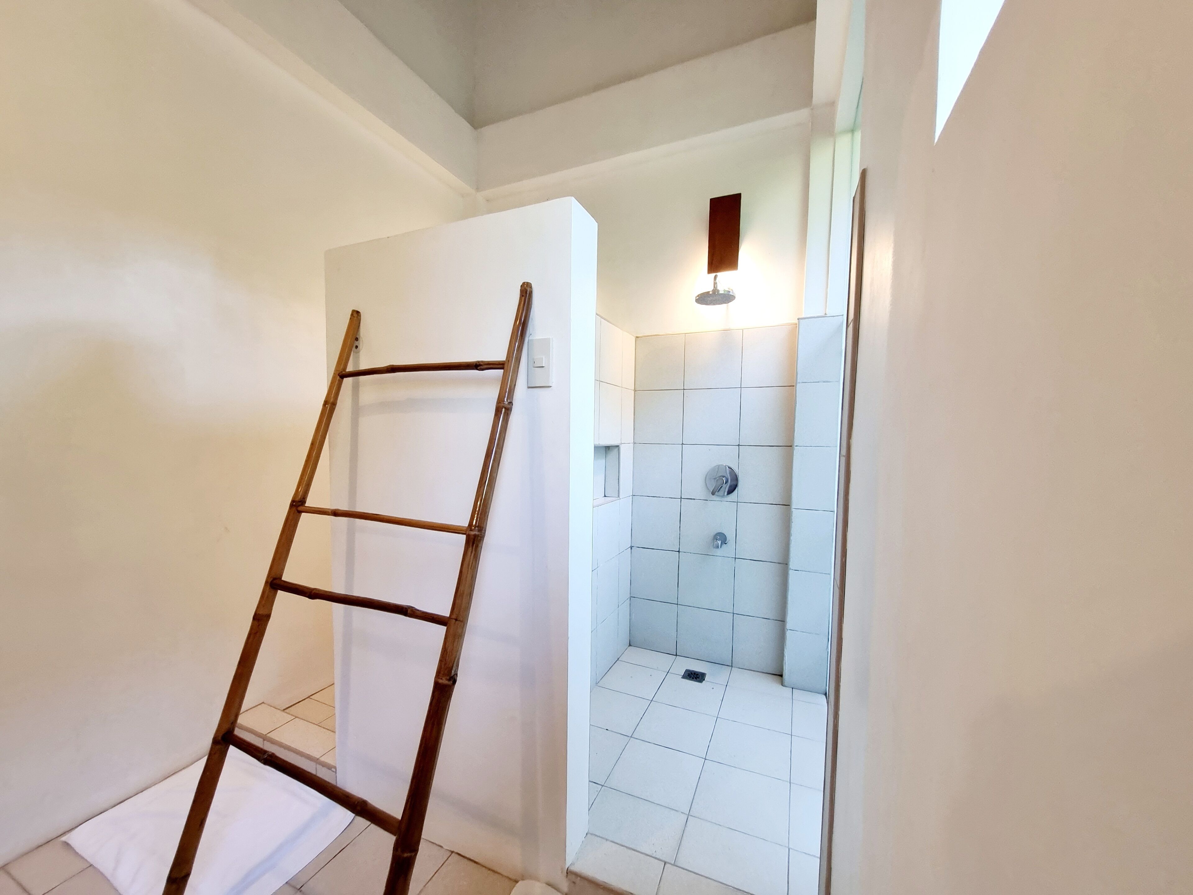 Une salle de bain avec une douche, des murs carrelés, une échelle en bois et un luminaire.