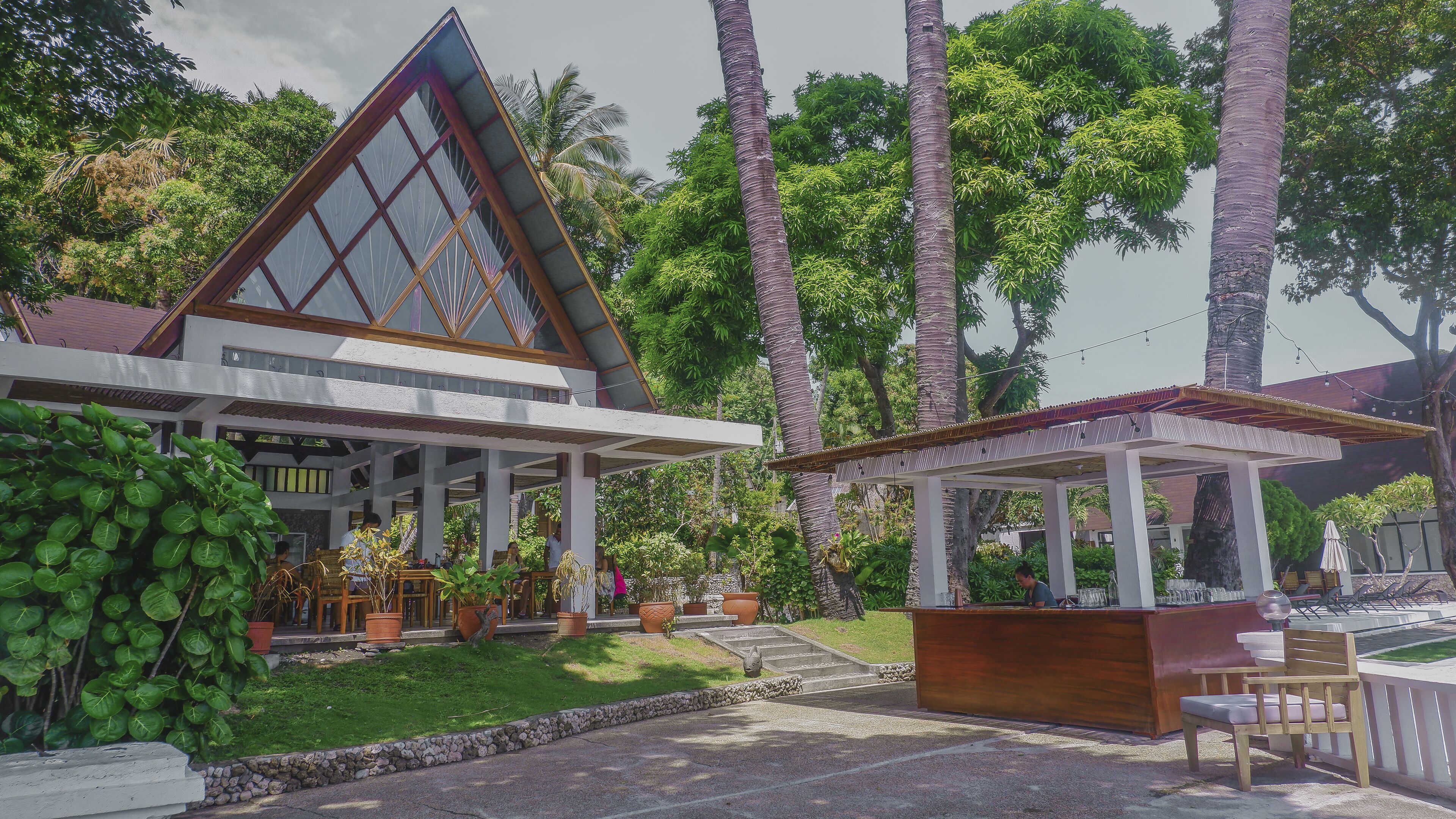 A modern building with a triangular roof, a covered outdoor seating area, and lush greenery.