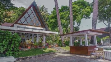 A modern building with a triangular roof, a covered outdoor seating area, and lush greenery.