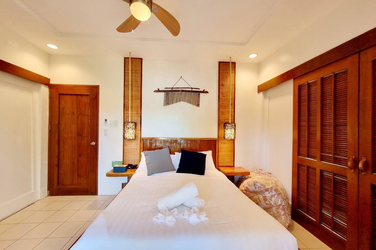 Une chambre d’hôtel équipée d’un lit, d’une armoire en bois, d’un ventilateur de plafond et d’appliques murales.