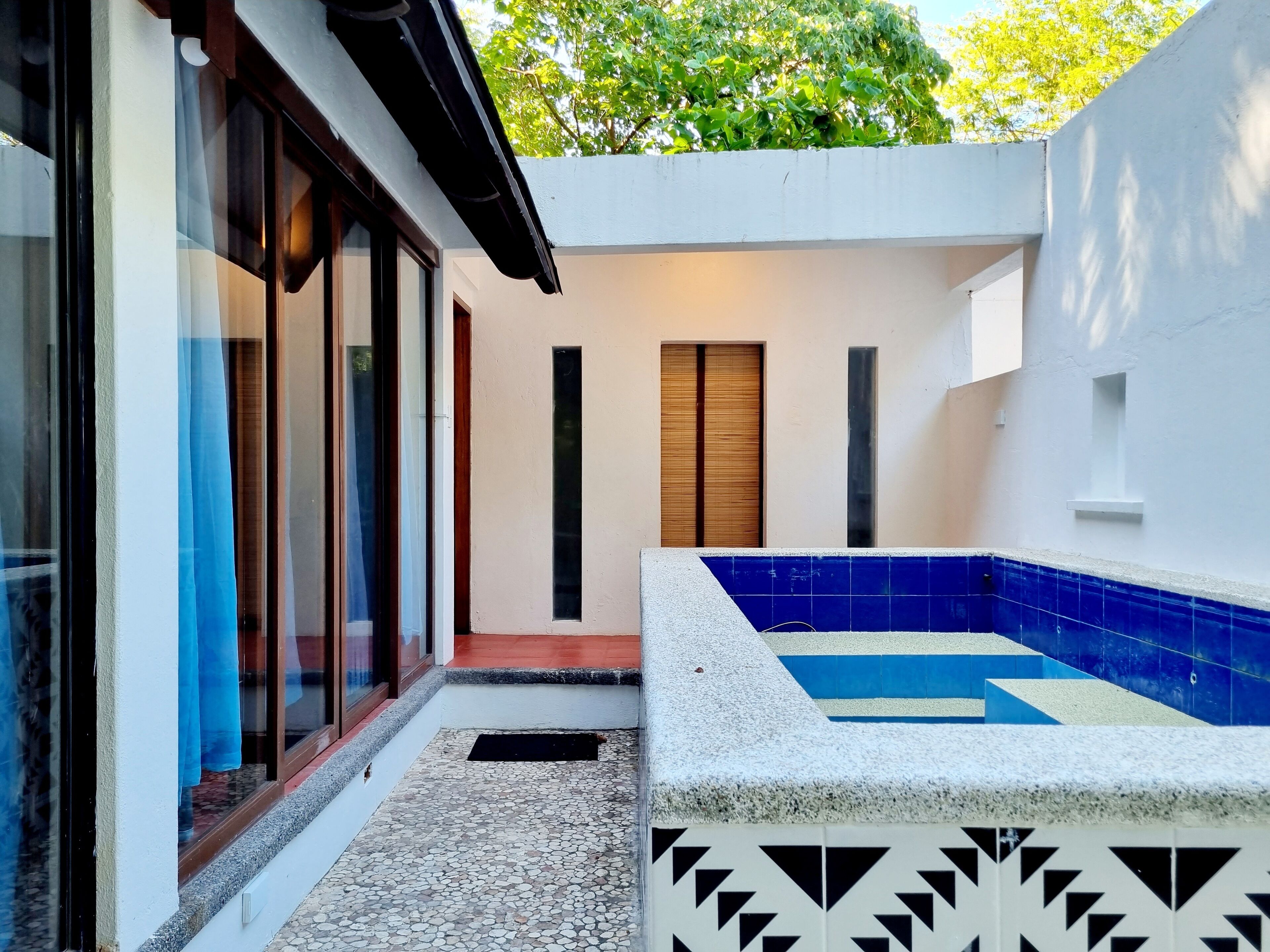 Un espacio exterior moderno con piscina, una puerta y un ventanal con cortinas.