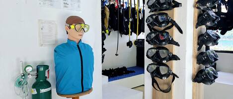 A room with a mannequin wearing a blue jacket and yellow goggles, a green oxygen tank, and several diving masks and equipment on shelves.