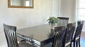Comedor con una gran mesa rectangular, seis sillas, una araña, un espejo y una planta en maceta.