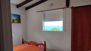 Ein Schlafzimmer mit einem Einzelbett, einem Fenster mit Jalousien, einer Tür und einem Deckenventilator.